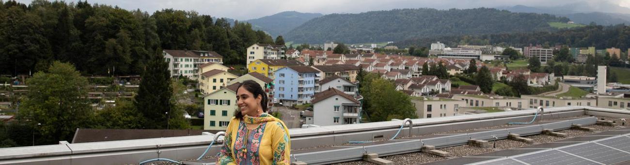 Ohio University student stands on balcony in Switzerland with mountains and buildings in the background