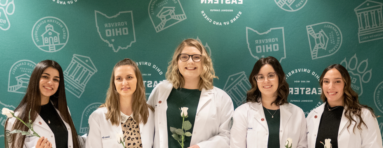Women in white coats standing in front of backdrop for photo.