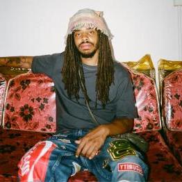 Earl Sweatshirt sitting on red floral couch with plastic covers